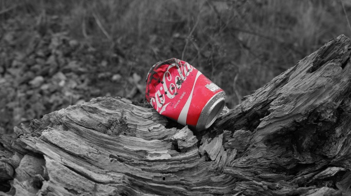 gedeukt Coca Cola blikje op boomstronk, gekleurd afvalblikje met achtergrond in grijstinten