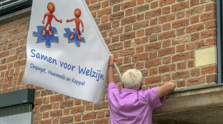 Gerard van Heusden en vlag met nieuw logo Stichting Welzijn Drempt, Hummelo en Keppel