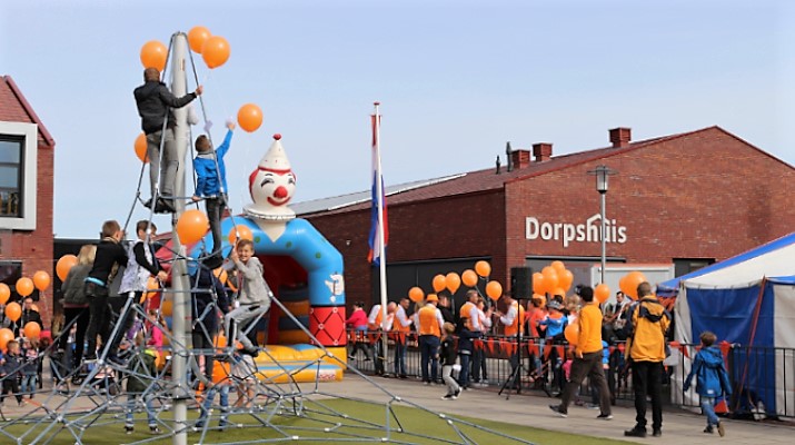 jong en oud met oranje ballonnen voor het dorpshuis op Koningsdag