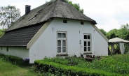 monumentaal wit boerderijtje met rieten dak met op de voorgrond groene beplanting