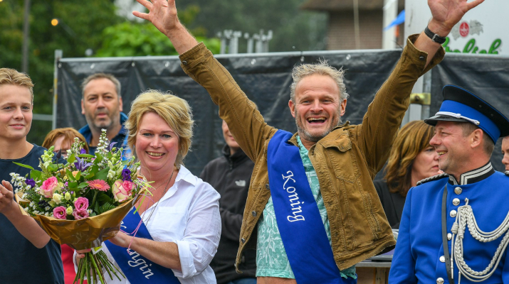 koning met handen in de lucht en koningin met bos bloemen