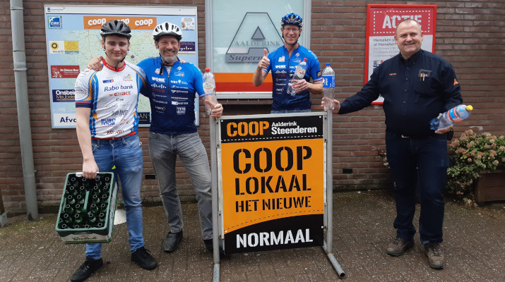 4 mannen waarvan 3 wielrenners bij supermarkt